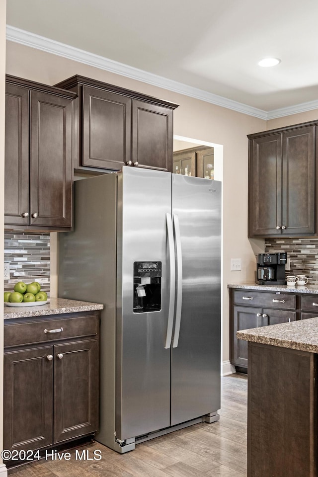 kitchen featuring dark brown cabinets, decorative backsplash, light wood finished floors, stainless steel fridge, and crown molding