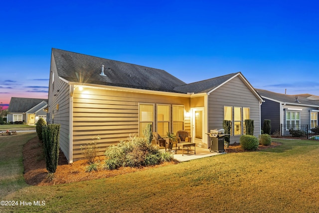 back of property at dusk with a yard and a patio