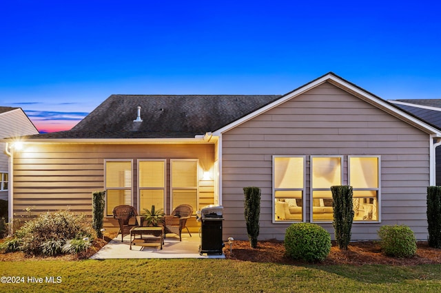 back of property at dusk with a yard and a patio