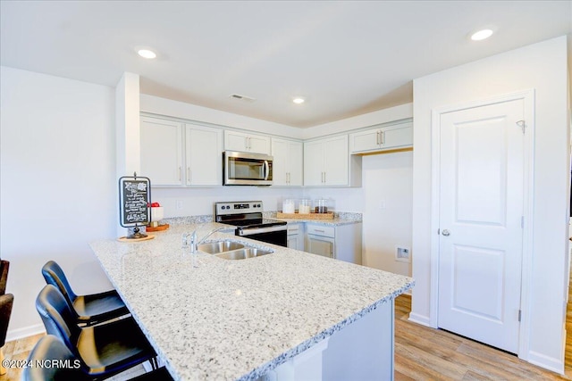 kitchen featuring light hardwood / wood-style floors, sink, kitchen peninsula, light stone counters, and appliances with stainless steel finishes