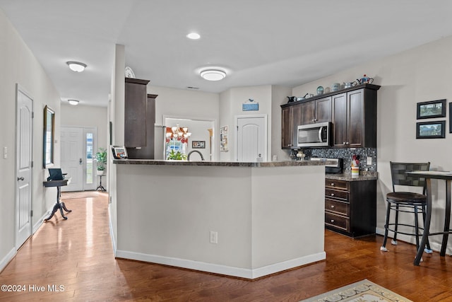 kitchen featuring dark brown cabinetry, stone countertops, tasteful backsplash, and dark wood-type flooring