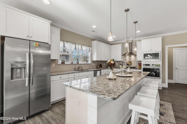 kitchen with wall chimney range hood, a center island, hanging light fixtures, appliances with stainless steel finishes, and white cabinets