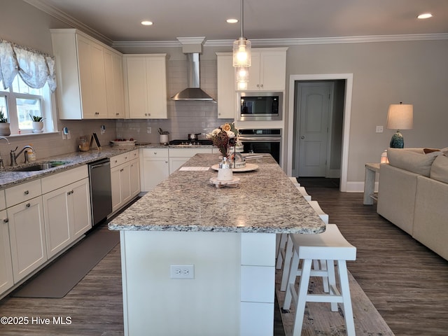 kitchen featuring appliances with stainless steel finishes, wall chimney exhaust hood, sink, and a center island