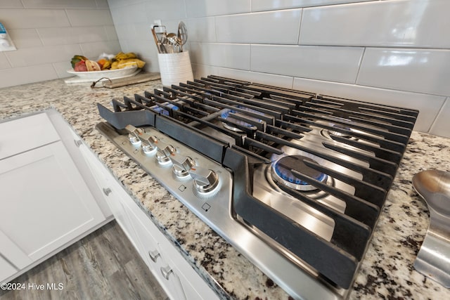 details featuring white cabinets, backsplash, light stone countertops, and stainless steel gas stovetop