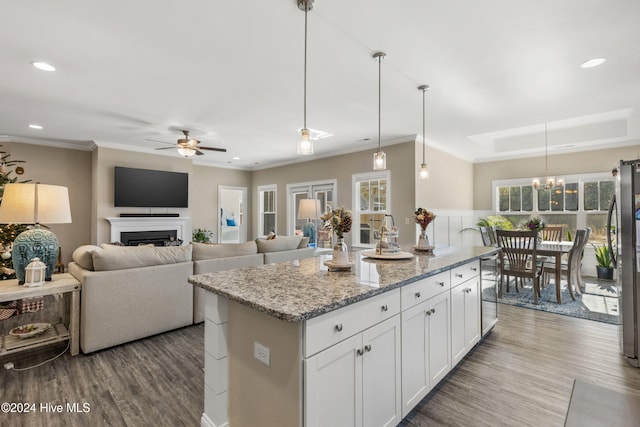 kitchen featuring ceiling fan with notable chandelier, white cabinets, a center island, decorative light fixtures, and light stone counters