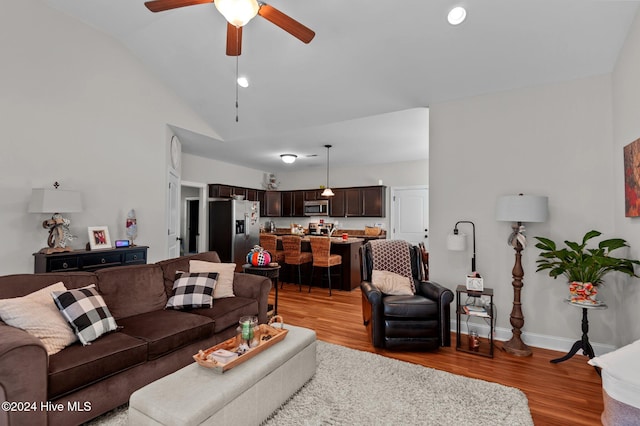 living room with ceiling fan, vaulted ceiling, and light wood-type flooring