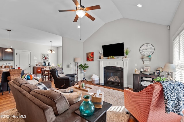 living room with ceiling fan with notable chandelier, light hardwood / wood-style flooring, and vaulted ceiling