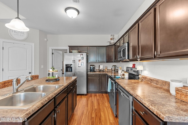 kitchen with light wood-type flooring, dark brown cabinets, stainless steel appliances, sink, and pendant lighting