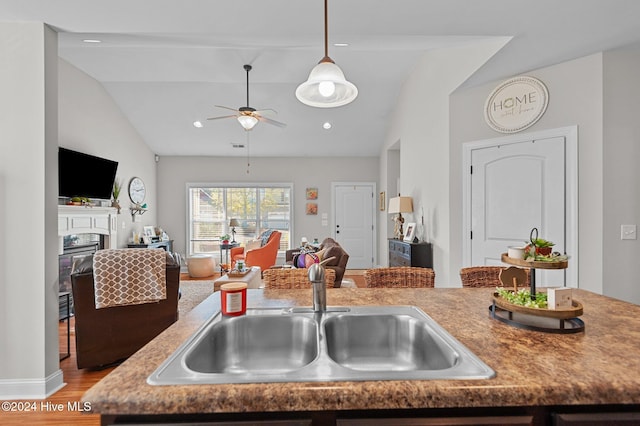 kitchen with vaulted ceiling, ceiling fan, sink, decorative light fixtures, and light hardwood / wood-style floors