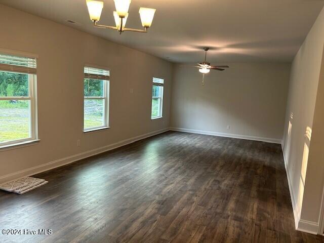 empty room with dark hardwood / wood-style flooring and ceiling fan with notable chandelier