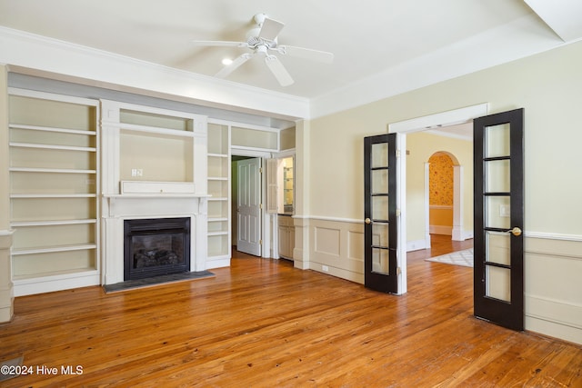 unfurnished living room featuring ceiling fan, wood-type flooring, built in features, and ornamental molding