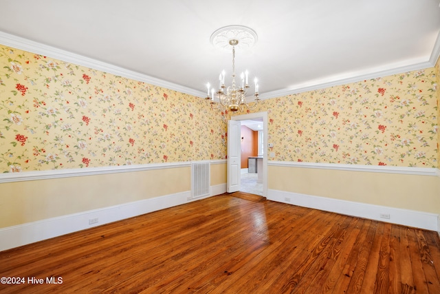 unfurnished room with hardwood / wood-style floors, an inviting chandelier, and crown molding