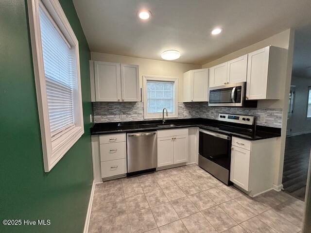 kitchen featuring a sink, tasteful backsplash, dark countertops, baseboards, and appliances with stainless steel finishes