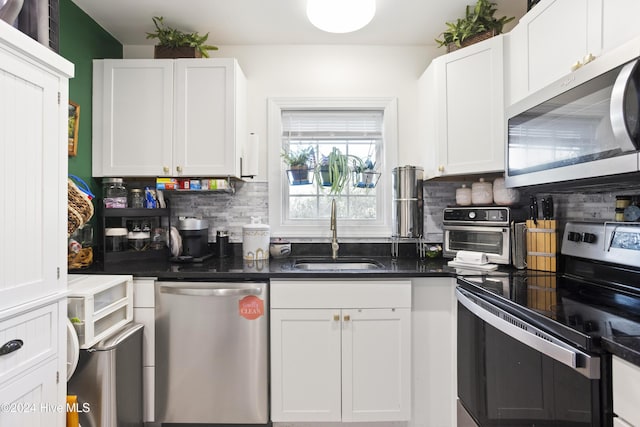 kitchen with a sink, stainless steel appliances, white cabinetry, dark countertops, and backsplash