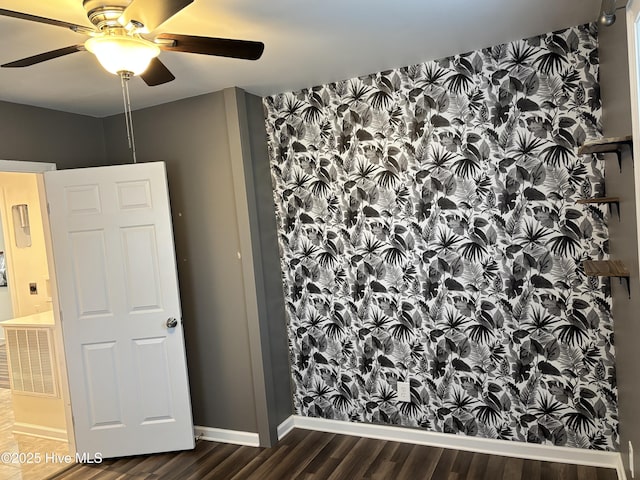 empty room with wallpapered walls, wood finished floors, visible vents, baseboards, and ceiling fan