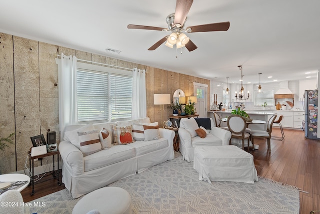 living room featuring hardwood / wood-style floors, ceiling fan with notable chandelier, and wood walls