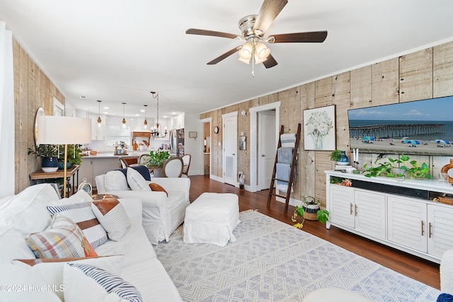 living room featuring ceiling fan with notable chandelier, wood walls, and dark hardwood / wood-style floors