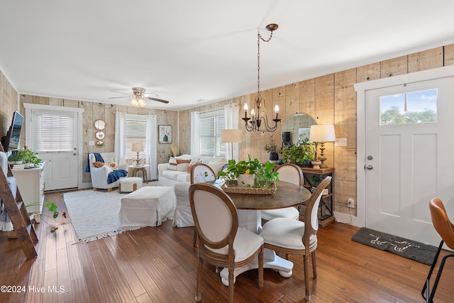 dining area with wood walls, wood-type flooring, and ceiling fan with notable chandelier