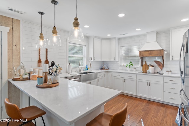 kitchen featuring kitchen peninsula, custom range hood, a kitchen bar, decorative light fixtures, and light wood-type flooring