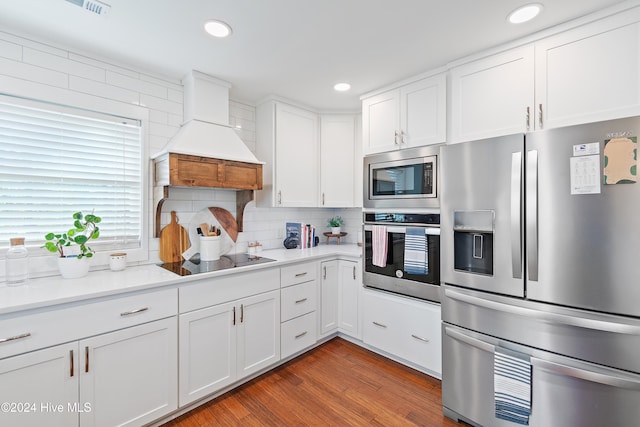 kitchen with stainless steel appliances, white cabinets, hardwood / wood-style floors, backsplash, and premium range hood