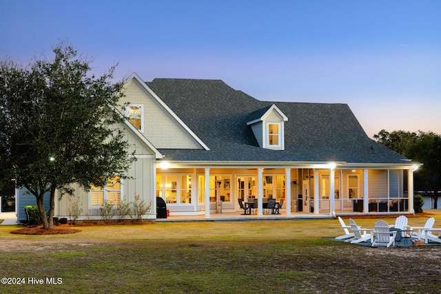 back house at dusk featuring a patio area and a lawn