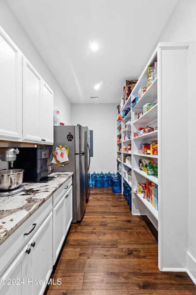 kitchen featuring light stone countertops, stainless steel fridge, white cabinetry, and dark wood-type flooring