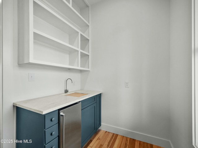 bar featuring light hardwood / wood-style flooring, blue cabinets, sink, and fridge