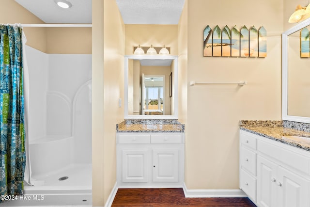 full bathroom with a textured ceiling, wood finished floors, two vanities, baseboards, and a shower stall