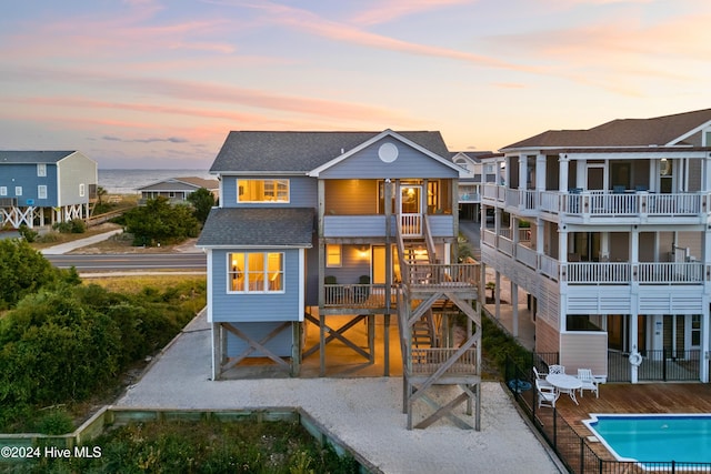 rear view of property with a fenced in pool, a shingled roof, stairway, a patio area, and a deck