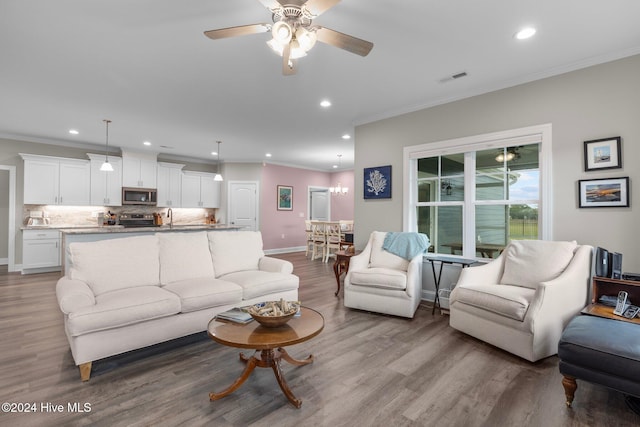 living room with crown molding, sink, wood-type flooring, and ceiling fan with notable chandelier