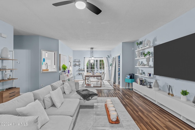 living room featuring ceiling fan with notable chandelier, a textured ceiling, and dark hardwood / wood-style flooring