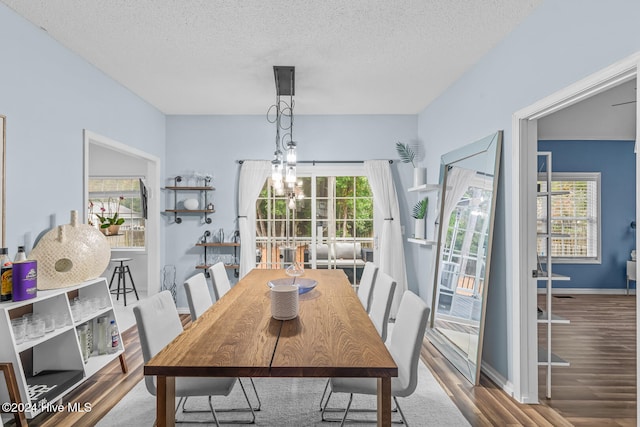 dining room featuring wood-type flooring, a textured ceiling, and a notable chandelier