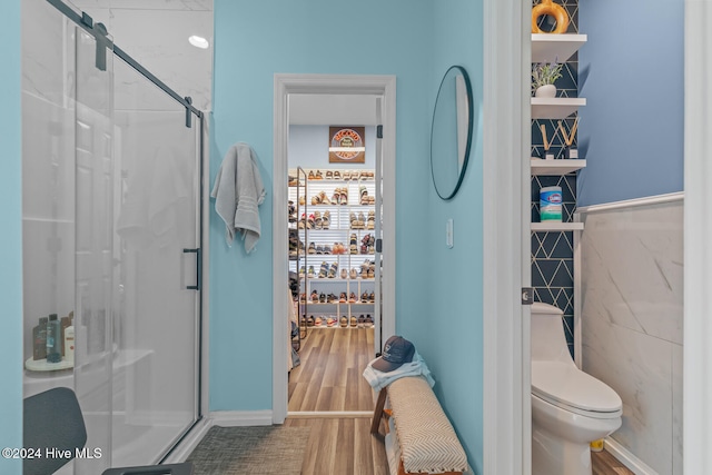 bathroom with hardwood / wood-style floors, a shower with door, toilet, and tile walls