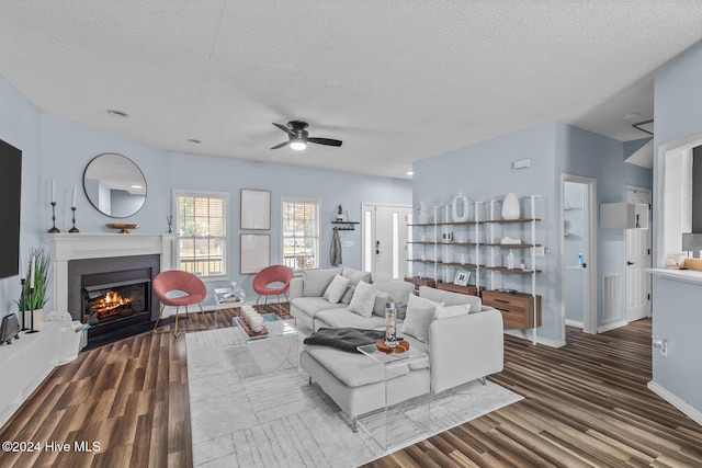 living room with dark wood-type flooring, a textured ceiling, and ceiling fan