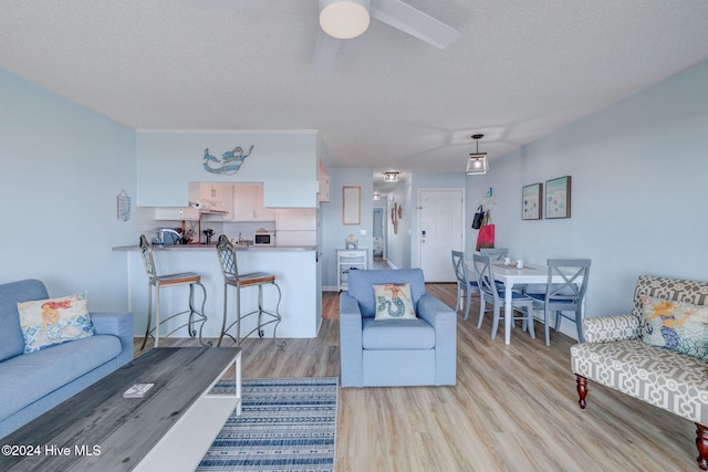 living room featuring a textured ceiling, light wood-type flooring, and ceiling fan