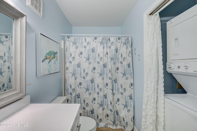 bathroom featuring curtained shower, hardwood / wood-style floors, stacked washing maching and dryer, vanity, and toilet