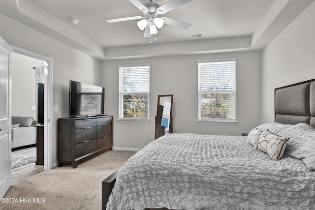 bedroom with a tray ceiling, multiple windows, light colored carpet, and ceiling fan