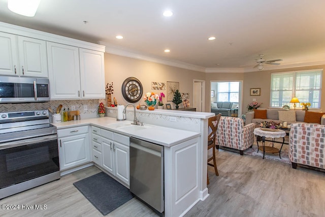 kitchen featuring stainless steel appliances, light wood-type flooring, sink, white cabinets, and kitchen peninsula