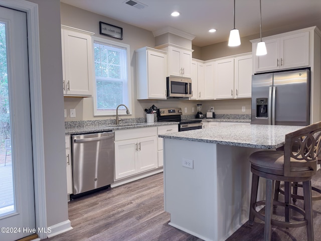 kitchen with light stone countertops, stainless steel appliances, a kitchen island, hardwood / wood-style floors, and white cabinetry