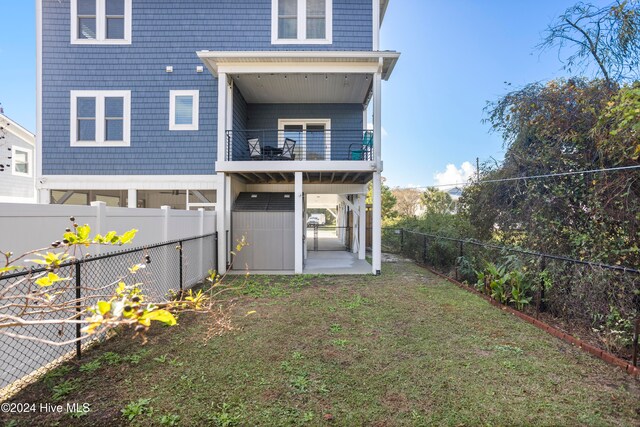 back of property featuring a balcony, a patio area, and a lawn