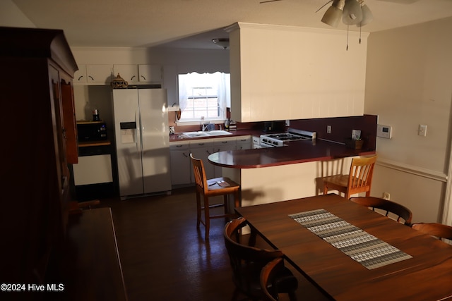 kitchen with white gas range, white cabinetry, sink, kitchen peninsula, and stainless steel fridge