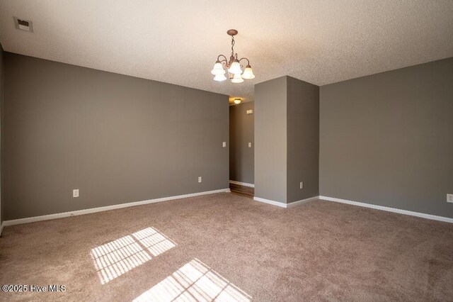 carpeted spare room featuring a textured ceiling and an inviting chandelier