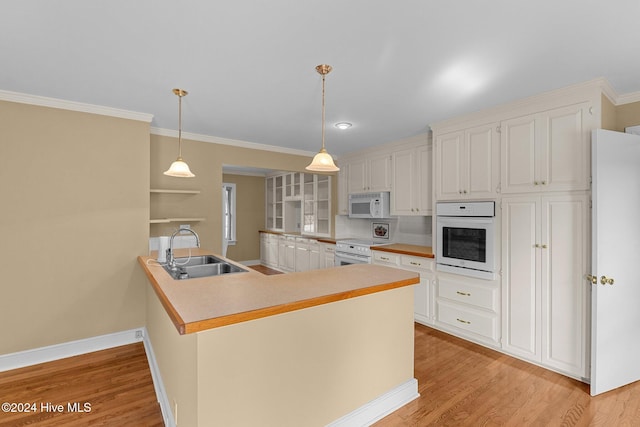 kitchen with decorative light fixtures, white appliances, sink, kitchen peninsula, and light hardwood / wood-style flooring