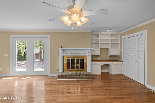 unfurnished living room with wood-type flooring, built in desk, crown molding, a brick fireplace, and ceiling fan