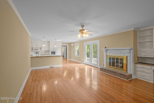 unfurnished living room featuring a brick fireplace, light hardwood / wood-style flooring, ceiling fan, and crown molding