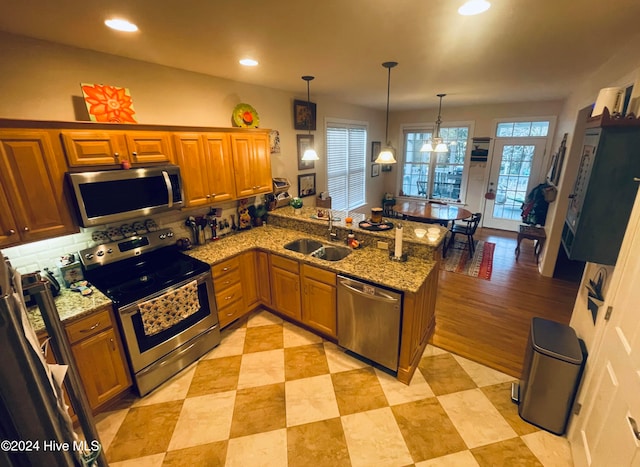 kitchen with kitchen peninsula, pendant lighting, stainless steel appliances, and sink