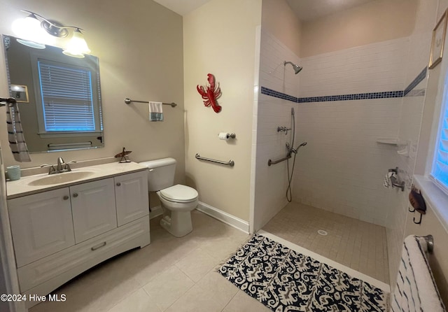 bathroom with toilet, a tile shower, tile patterned flooring, and vanity