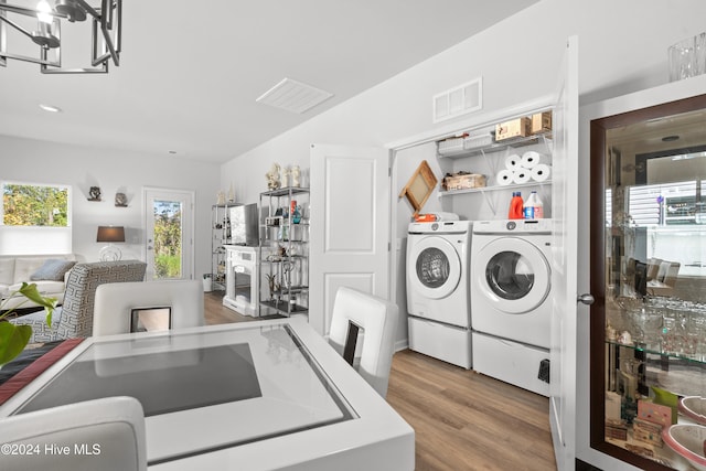 clothes washing area with washing machine and dryer, wood-type flooring, and an inviting chandelier