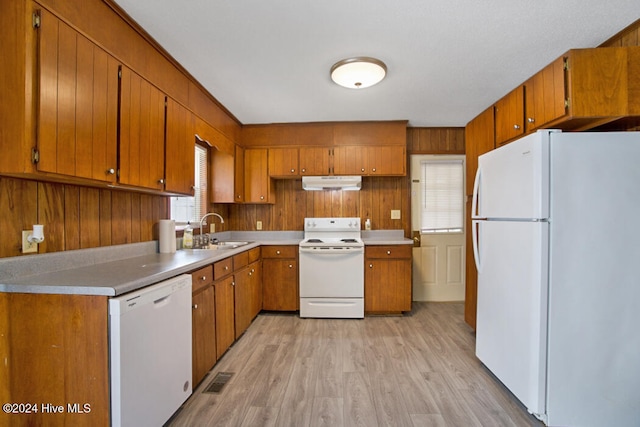 kitchen with white appliances, wooden walls, sink, and light hardwood / wood-style flooring