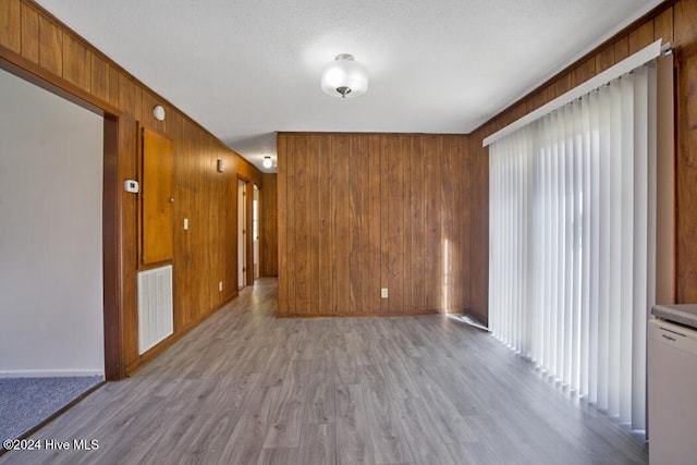 spare room with light wood-type flooring, wooden walls, and a textured ceiling